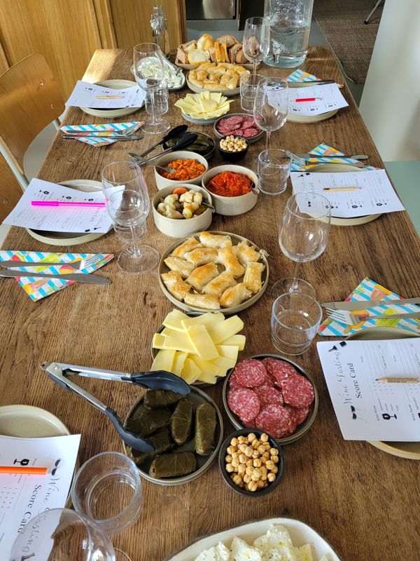 Tafel vol Macedonische mezze: kaas, olijven, gevulde bladerdeeghapjes, wijnglazen en score cards